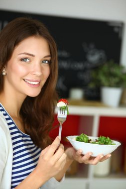 Genç bir kadın salata yiyor ve karışık bir şey tutuyor.