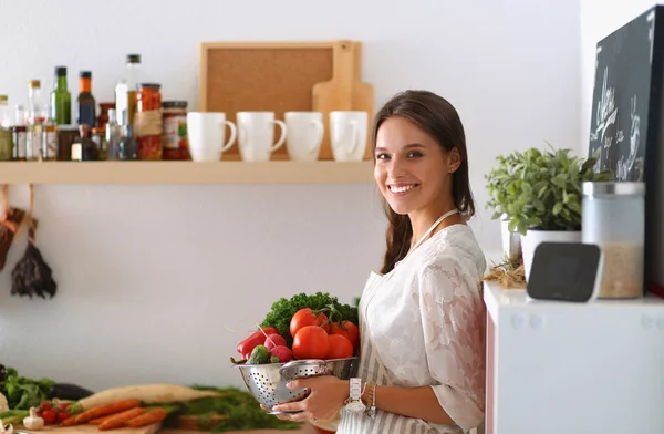 Mujer joven sonriente sosteniendo verduras de pie en la cocina —  Fotos de Stock