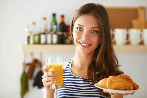 Jovem com copo de suco e bolos de pé na cozinha — Fotografia de Stock