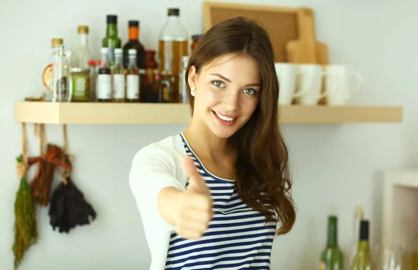 Young woman standing near desk in the kitchen and showing ok — Stock Photo, Image