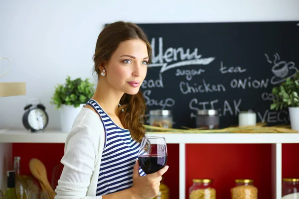 Mujer bonita bebiendo un poco de vino en casa en la cocina —  Fotos de Stock