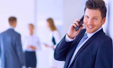 Ofisteki genç iş adamının portresi. Arka planda meslektaşları var ve cep telefonu kullanıyor.