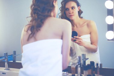 Genç bir kadın aynaya bakıyor ve makyaj yapıyor.