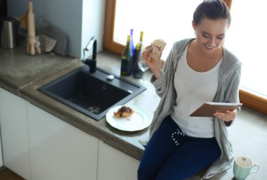 Mutfakta dijital tablet kullanan güzel genç bir kadın.