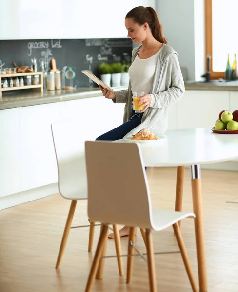 Young woman with orange juice and tablet in kitchen — Stock Photo, Image