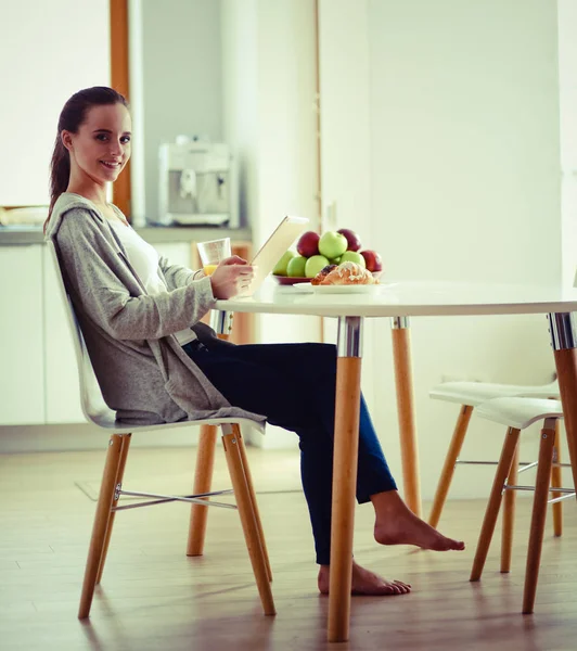 Ung kvinna med apelsinjuice och tablett i köket — Stockfoto