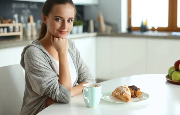 Kobieta, picie herbaty z słodkiego rogalika na stole w kuchni — Zdjęcie stockowe