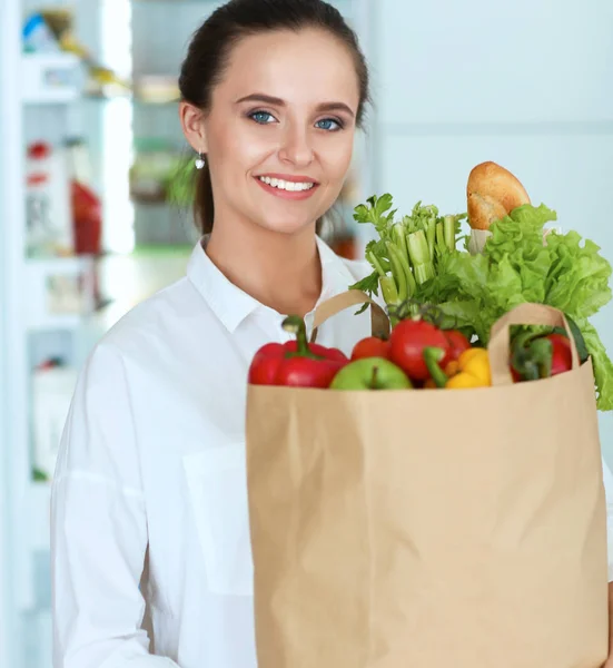 Młoda kobieta trzyma torbę na zakupy z warzywami.Stojąc w kuchni — Zdjęcie stockowe