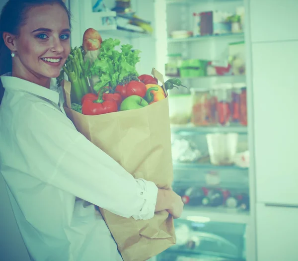 Ung kvinna som håller i matkassen med grönsaker.Står i köket — Stockfoto