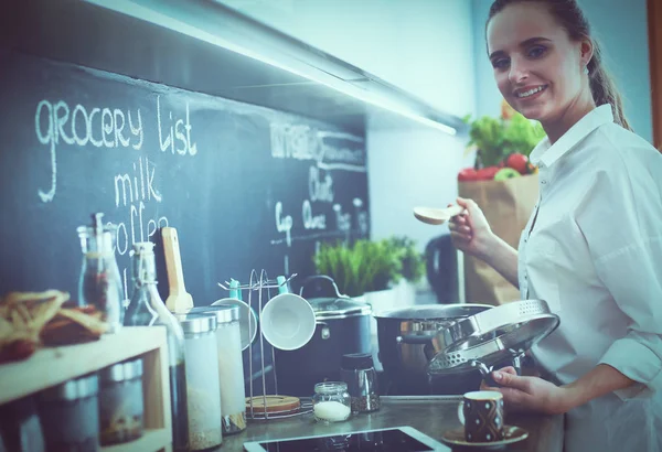 Young woman standing by the stove in the kitchen — Stock Photo, Image