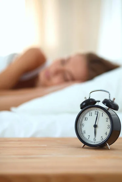 Joven mujer dormida y despertador en el dormitorio en casa —  Fotos de Stock