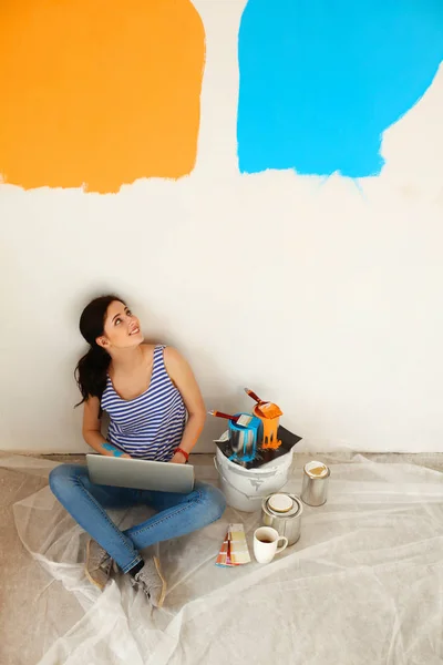 Portret van de jonge vrouw tijdens het schilderen van nieuw appartement, zitten met laptop — Stockfoto