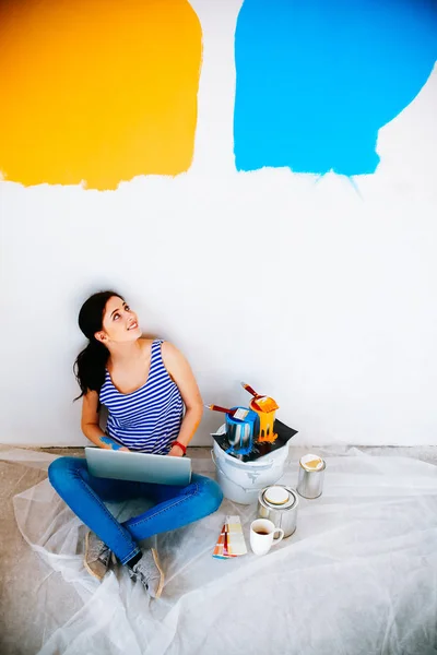 Portret van de jonge vrouw tijdens het schilderen van nieuw appartement, zitten met laptop — Stockfoto