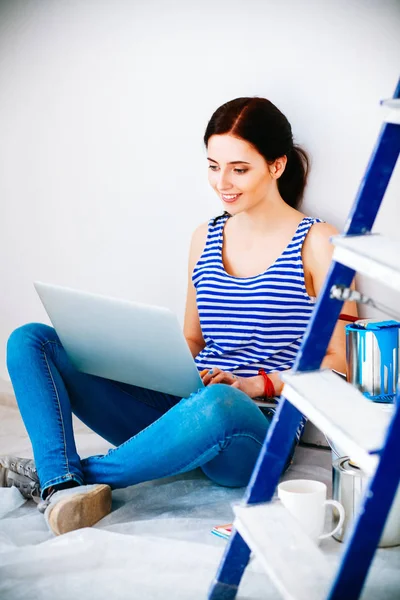 Portret van de jonge vrouw tijdens het schilderen van nieuw appartement, zitten met laptop — Stockfoto