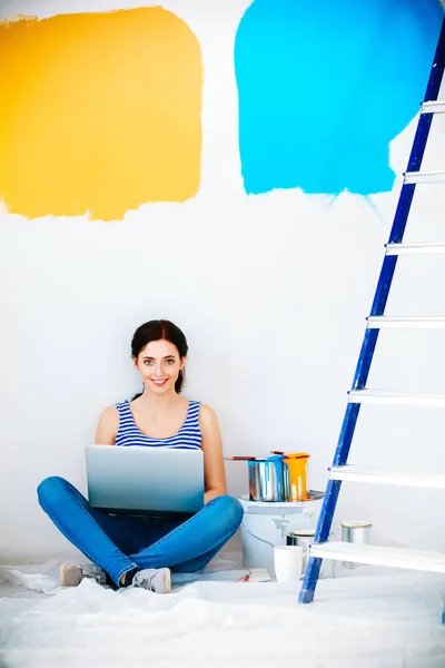 Portret van de jonge vrouw tijdens het schilderen van nieuw appartement, zitten met laptop — Stockfoto