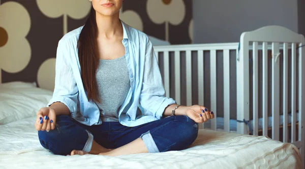 Mujer joven sentada en la cama cerca de cuna de los niños —  Fotos de Stock