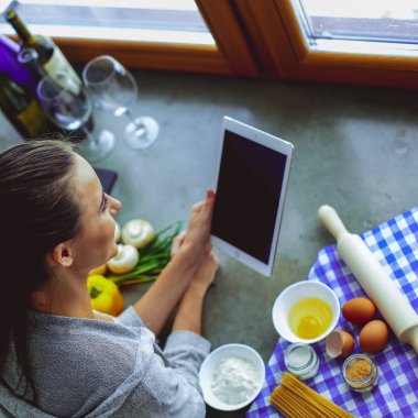 Tablette tarifi takip eden bir kadın evde yemek pişiriyor.