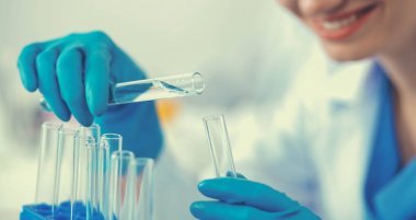 Kadın araştırmacı, beyaz arka planda izole edilmiş ilaç şişeleri ve mataralarla çevrili.