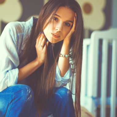 Yatakta çocuk karyolası yakın oturan genç yorgun kadın