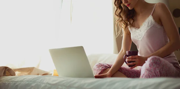 Joven hermosa mujer sentada en la cama con portátil —  Fotos de Stock