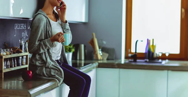 Kvinna med mobiltelefon sitter i moderna kök — Stockfoto