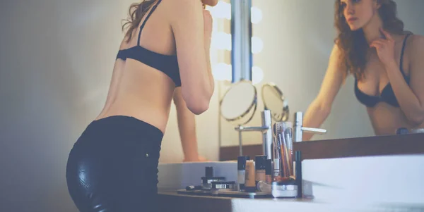 Mujer joven mirándose en el espejo en el baño — Foto de Stock