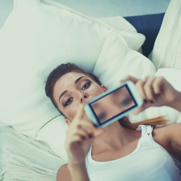 Счастливая брюнетка фотографирует себя со своим мобильным телефоном в спальне — стоковое фото