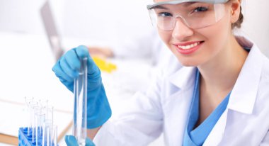 Kadın araştırmacı, beyaz arka planda izole edilmiş ilaç şişeleri ve mataralarla çevrili.