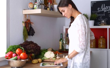 Mutfakta yemek yapmak için tablet bilgisayar kullanan genç bir kadın.