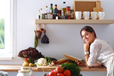 Mutfakta yemek kitabı okuyan genç bir kadın yemek tarifi arıyor.