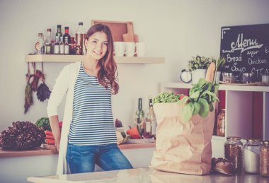 Genç bir kadın mutfakta duruyor.