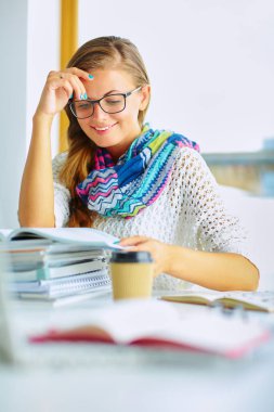 Kitapların arasında masa başında oturan genç bir kadın.