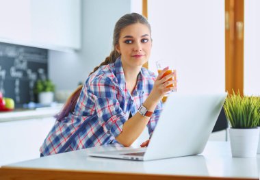 Mutfakta dizüstü bilgisayar kullanan genç bir kadın.