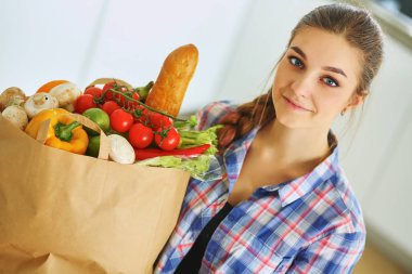 Elinde sebzeli alışveriş torbası tutan genç bir kadın.