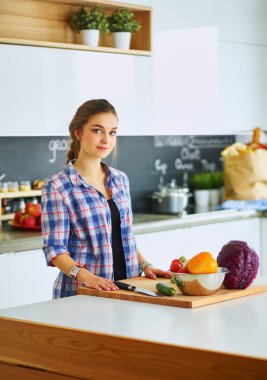 Masanın yanındaki mutfakta sebze doğrayan genç bir kadın.
