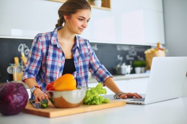 Masanın yanındaki mutfakta sebze doğrayan genç bir kadın.