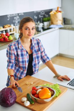 Masanın yanındaki mutfakta sebze doğrayan genç bir kadın.