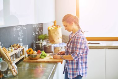 Masanın yanındaki mutfakta sebze doğrayan genç bir kadın.