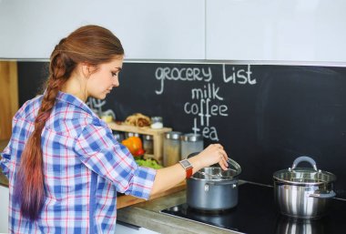 Mutfakta sobanın yanında duran genç bir kadın.