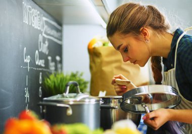 Mutfakta sobanın yanında duran genç bir kadın.