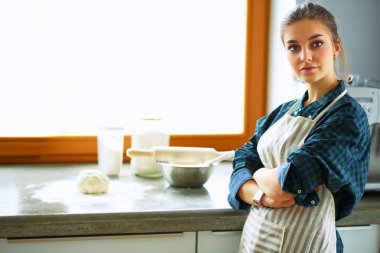 Güzel bir kadın mutfakta pasta pişiriyor. Masanın yanında duruyor.