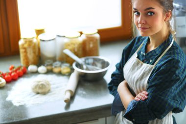 Güzel bir kadın mutfakta pasta pişiriyor. Masanın yanında duruyor.
