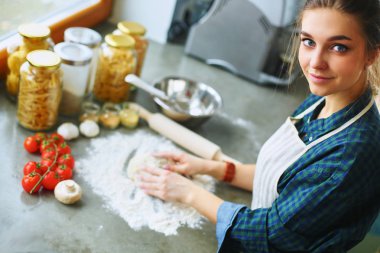 Güzel bir kadın mutfakta pasta pişiriyor. Masanın yanında duruyor.