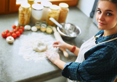 Güzel bir kadın mutfakta pasta pişiriyor. Masanın yanında duruyor.
