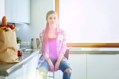 Güzel bir kadın mutfakta pasta pişiriyor. Masanın yanında duruyor.