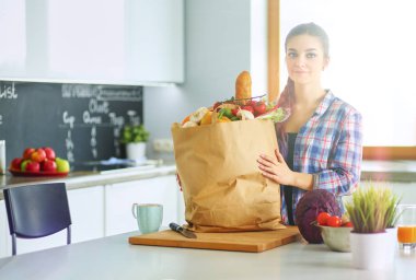 Güzel bir kadın mutfakta pasta pişiriyor. Masanın yanında duruyor.