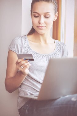 Genç ve güzel bir kadın evde dizüstü bilgisayar kullanıyor.