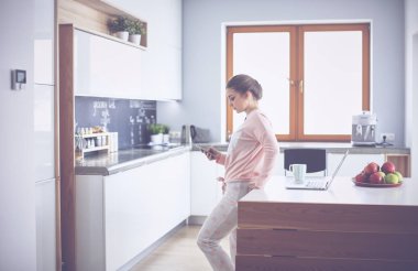 Cep telefonu ayakta modern mutfak kullanan kadın