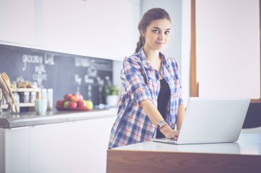 Mutfakta dizüstü bilgisayar kullanan genç bir kadın.