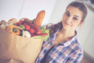 Elinde sebzeli alışveriş torbası tutan genç bir kadın.